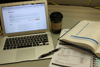 Laptop next to an open textbook and notebook